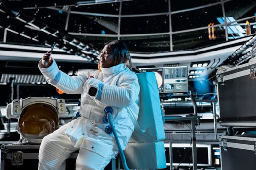 Smiling astronaut doing remote videocall with command center on Earth using smartphone. Jolly African american woman in orbit station chatting with ground control researchers using phone photo