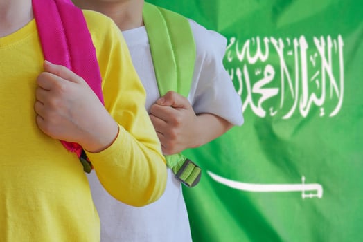 Two kids with satchels background of Saudi arabia flag photo