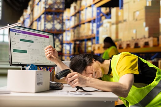 Tired employee deals with burnout and takes a nap with scanner in his hand, scanning shipping labels at warehouse desk. Order fulfillment and inventory management in a long shift. photo
