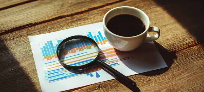 The magnifying glass and coffee cup on financial charts on a wooden desk photo