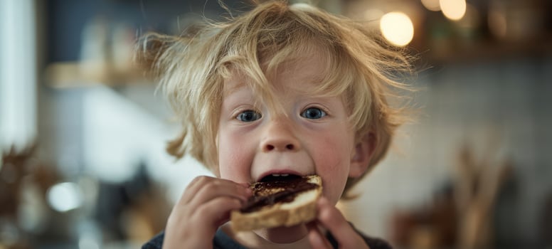 The boy eating chocolate-covered toast with messy face and playful kitchen moment photo