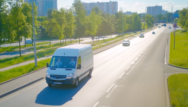 Delivery van driving along a sunny urban road with green trees lining the street photo