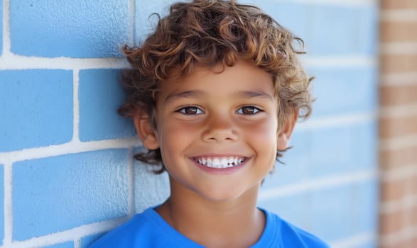 Happy boy smiles, leaning on blue brick wall photo