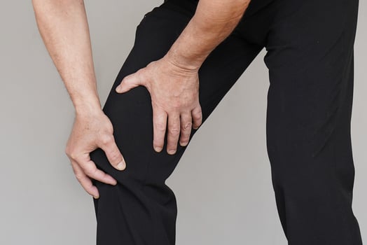 Elderly man feeling joint pain, having health issues and touching leg with hands isolated on grey background photo