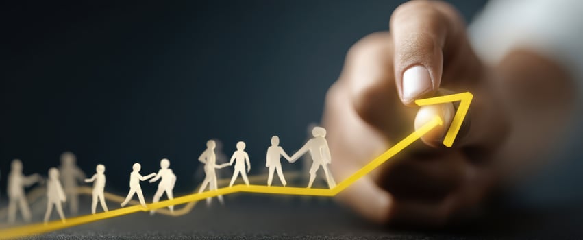 The hand drawing an upward yellow arrow guiding paper cutout people toward growth photo