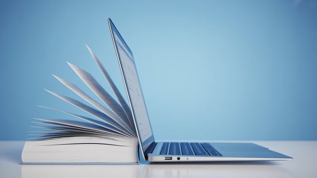 A creative composition of a book and a laptop on a light blue background, symbolizing knowledge and technology. photo