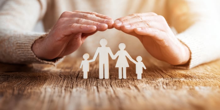 The hands providing protection over a family symbol made of paper cutouts. photo