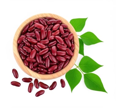 a wooden bowl full of red beans surrounded by green leaves on a white background. The beans scattered nearby emphasize the natural and healthy character of the still life. photo