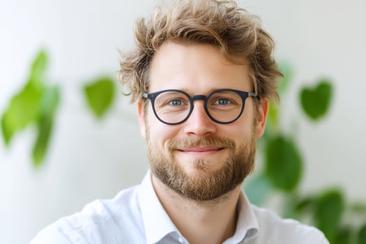 Smiling man with glasses in a bright indoor setting surrounded by greenery photo