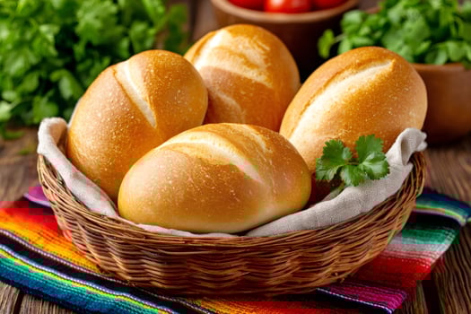 Freshly baked bolillo rolls resting in a wicker basket on a vibrant mexican blanket photo