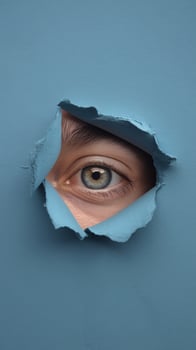 A close-up of a blue eye peering through a torn blue paper, creating an intriguing visual effect. photo