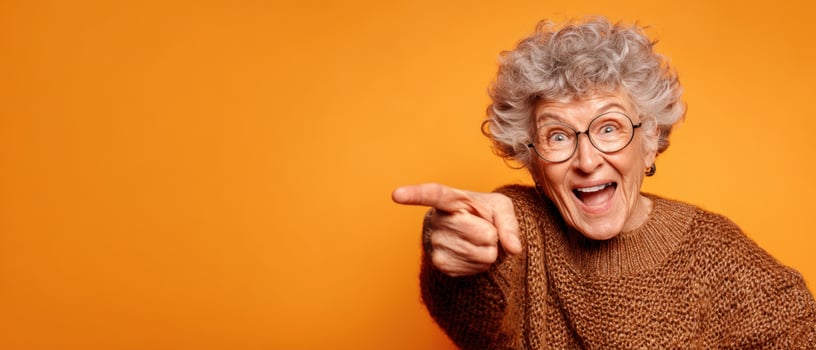The joyful elderly woman playfully pointing and expressing happiness against an orange background. photo