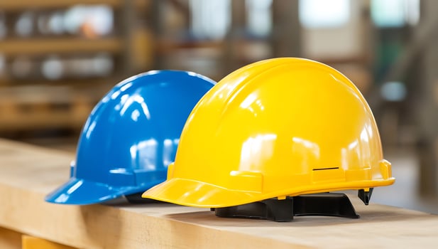 Blue and yellow hard hats on wood beam, factory background, safety photo