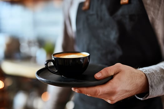 Barista Serving Cappuccino in Black Cup on Plate photo