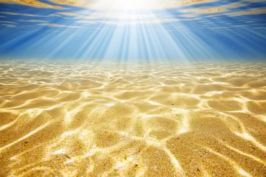 Underwater sunlit ocean sand, background blue sky, summer vacation photo