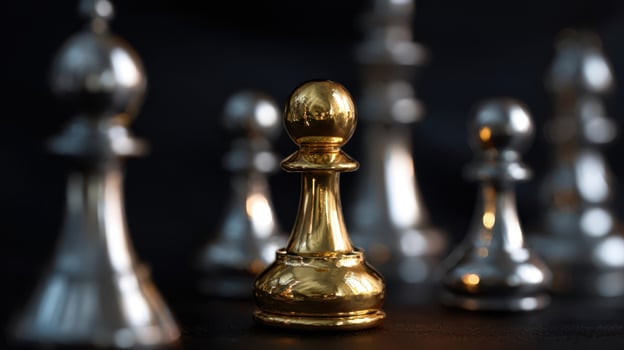 The golden pawn stands out among silver chess pieces in dramatic lighting. photo