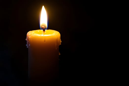 A single yellow candle is lit in the dark photo