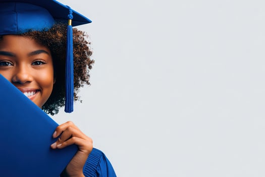 A young woman in a blue graduation gown is smiling broadly while holding her diploma. Her curly hair and the graduation cap accentuate her happiness. This moment celebrates her academic achievement. photo