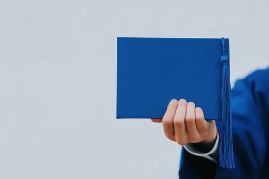 A person holding a blue graduation cap with a tassel, symbolizing the completion of their academic journey. The background is neutral, enhancing the celebratory moment. photo
