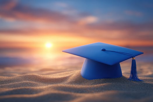 A blue graduation cap rests on golden sand with a stunning sunset in the background. The scene captures the essence of achievement and new beginnings by the sea. photo
