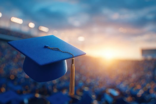 A blue graduation cap with a gold tassel floats against a stunning sunset backdrop in a packed stadium. Families and graduates gather to celebrate the achievements of the day. photo
