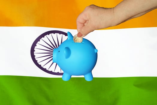 Hand putting coin to piggy bank on India flag background photo