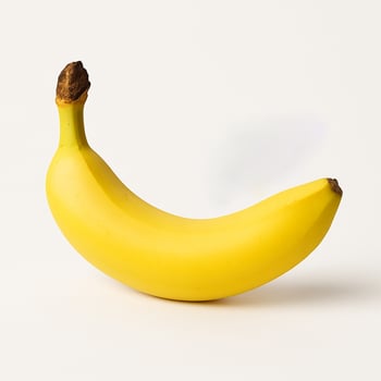 Single ripe yellow banana with stem, curved shape, isolated on a clean white background with soft studio shadow. Minimal food image for recipes, nutrition and vegan themes. photo