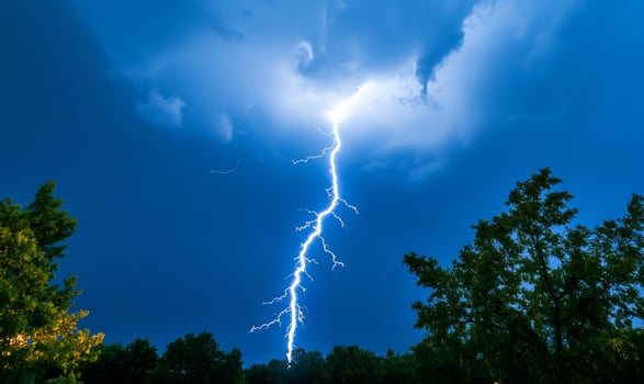 Lightning strike over trees at night, dramatic weather photo