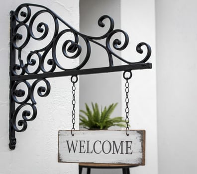 Ornate black metal bracket supports a rustic white welcome sign photo