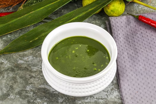 A bowl of green sauce next to some leaves photo