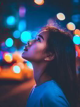 Young Woman Gazing Upwards at Night, Illuminated by City Lights. photo