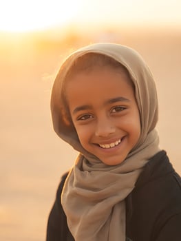 Happy Young Girl in Headscarf Smiles at Sunset. A close up portrait of a smiling child outdoors in warm golden light. photo