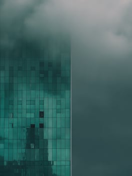 Modern building facade with teal glass panels partially obscured by fog, creating an abstract architectural image. photo