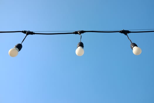 Vintage glowing light bulbs hang from a thin wire in the air and blu sky in bright day photo