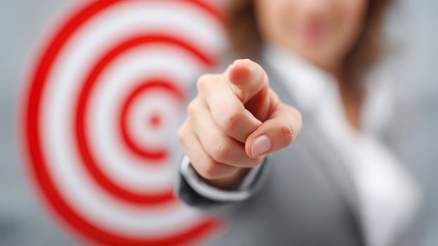 Businesswoman pointing directly at the camera with a target in the background, symbolizing focus, leadership, and personal responsibility photo