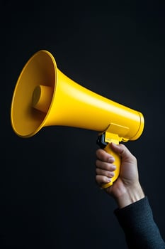 Close up of hand holding vibrant yellow megaphone against dark background symbolizing announcement and communication photo