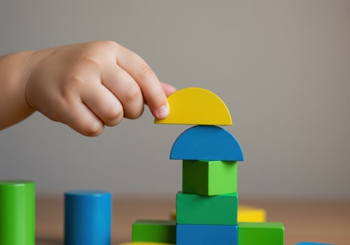 A childs hand places a yellow halfcircle block on top of a colorful tower photo