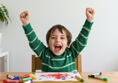 A young boy celebrates his artistic creation with raised hands and a big smile photo