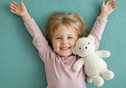 Happy young girl with blonde hair holding a teddy bear, arms raised in excitement photo