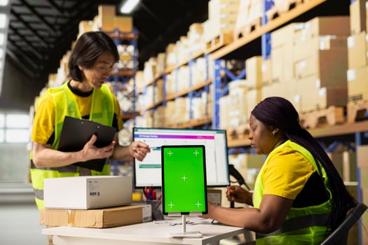 Diverse staff warehouse workers next to green screen monitor. Managing shipping labels, barcode scanner data or e-commerce inventory tracking systems in industrial warehouse. photo