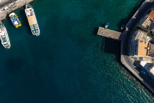 Aerial view of Agios Nikolaos, Crete, showing turquoise waters, docked boats, a curved road, and light roofed buildings near the shoreline. photo