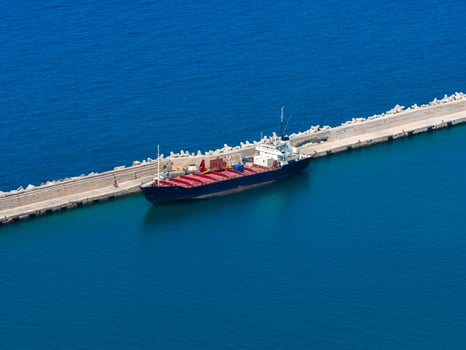 Aerial view of a dark blue cargo ship with red containers docked at a concrete pier in vibrant blue waters near Crete Island, Greece. photo