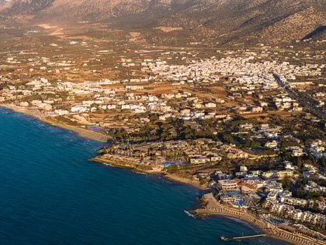 Aerial view of Stalida, Crete, showing sandy beaches, resorts, white buildings, and greenery by the Aegean Sea with rugged mountains in the background. photo