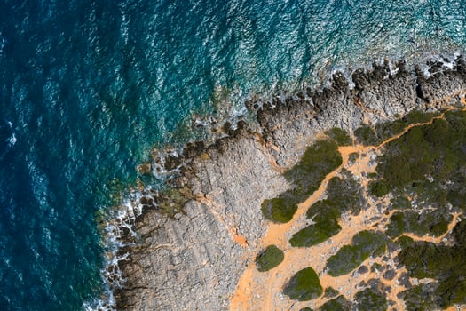 Aerial view of a rocky coastline with vibrant blue waters, green vegetation, and orange brown earth near Voulisma Beach in Crete. photo