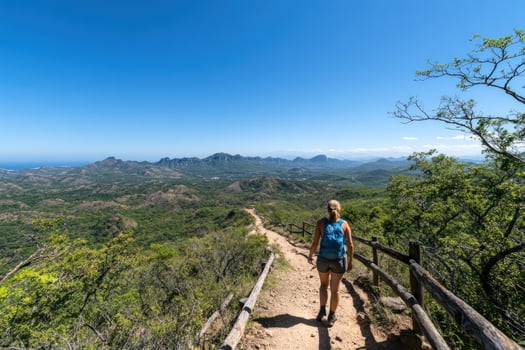 Woman hikes along a scenic trail with a beautiful view of mountains and ocean in the distance. photo