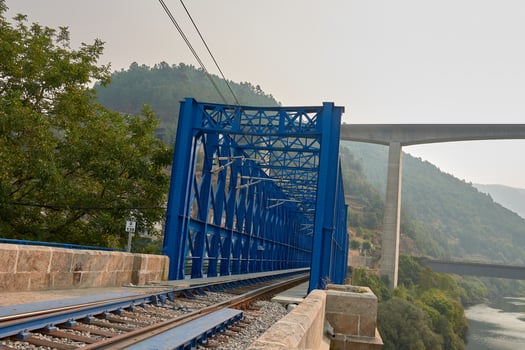Blue railway bridge in Peares, Galicia, with train tracks and green mountains in the background in a rural landscape photo