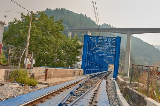 Train tracks crossing a blue iron bridge in Peares, Galicia, with green hills in the background photo
