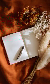 Cozy autumn aesthetic featuring an open blank notebook a stylish pen and elegant dried flowers on a warm toned textured fabric providing inspiration for creative writing or photo