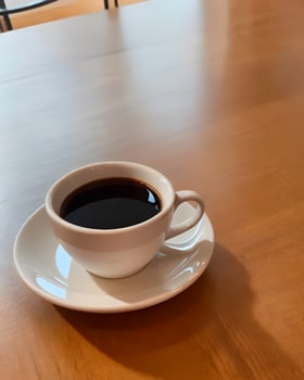 A white cup of coffee sits on a wooden table, ready for a morning treat. photo