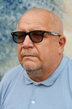 Portrait of Caucasian gray haired man in blue shirt and sunglasses on light background. photo